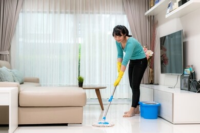 attractive young asian woman mopping tile floor at living room while doing cleaning at home during staying at home using free time about their daily housekeeping routine.