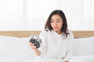portrait of young beautiful asian bad moody woman shocked looking at the clock and sitting in white bed while wake up late in the morning.