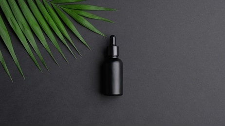 black dropper bottle mockup and palm leaf on black background. flat lay, top view. herbal cosmetic, natural organic beauty product, essential oil packaging design. 
