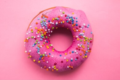 homemade circle donut with pink icing and rainbow sprinkles on the trendy soft pink background situated in the center of image. doughnut pastry.
