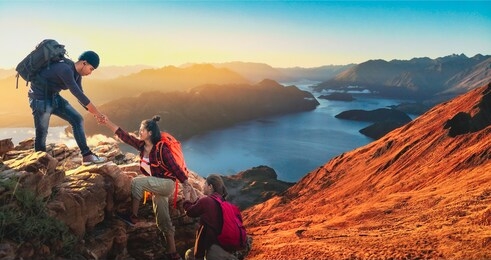 young asian three hikers climbing up on the peak of mountain. people helping each other hike up a mountain at sunlight. giving a helping hand. climbing. helps and team work concept