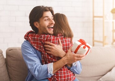 emotional young father hugging his little daughter, holding gift box at home, free space