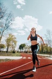 girl runs on a treadmill on the street. red running track. blue sky . street sport. young athletic girl in leggings, sneakers and a top. track and field athlete.