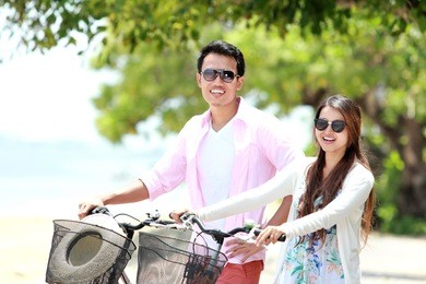portrait of happy asian young couple with bicycle on the beach having fun together