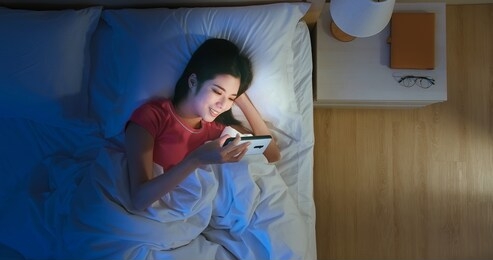 top view of asian woman use smartphone to watch video on bed at night
