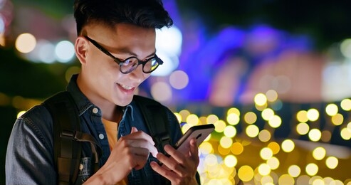 asian young man use smart phone outdoor and play interesting mobile game in the evening