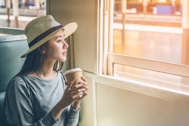 happy young asian cute woman sitting, holding coffee cup and looking outside the window train. travel summer and holiday concept.