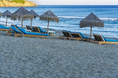 luxurious beach chairs & umbrellas by an empty sandy beach. evening view of wooden deck chairs with blue mattresses below bamboo sun protect umbrellas without crowd at mykonos greece paradise beach.