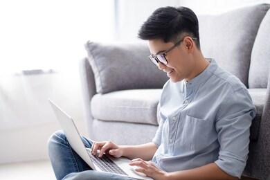 young asian people work on laptops on the floor, beside the sofa at home.