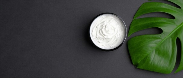 jar with cosmetic cream and tropical monstera leaf on black background. natural organic beauty product for body, hand, face skin treatment. flat lay, top view. skincare concept.