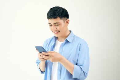 relaxed young casual man reading text message on mobile phone isolated over white studio background.