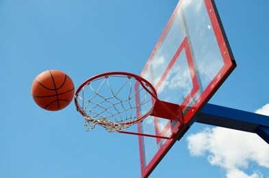 a basketball ball flies into a ring on an open field against the sky