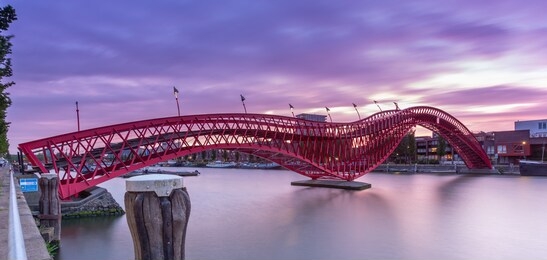 python bridge or high bridge in amsterdam connectiong the stuurmankade and panamakade. the iron bridges is shaped like a red snake during sunset. long exposure  - panoramic view.