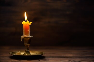 close up of burning old candle with vintage brass candlestick on wooden background in minimalist room interior 
