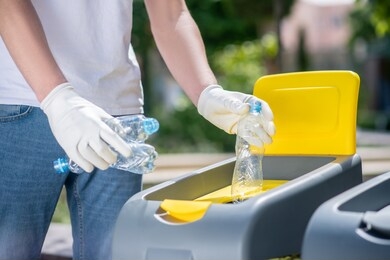 waste sorting. close-up of male hands in protective gloves throwing open plastic bottles into waste container