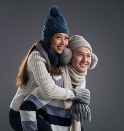 isolated image of a young couple in winter wearing piggybacking over a grey background 