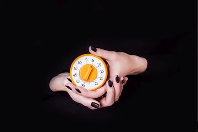 female hands holding round orange kitchen timer on a black background. copy space, time concept
