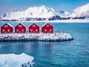 traditional red wooden houses on the shore of offersoystraumen fjord. beautiful winter scene of vestvagoy island. picturesque morning view of lofoten islands, norway, europe.  life over polar circle.