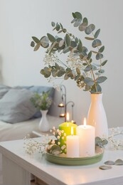 burning candles and eucalyptus in  vase in white bedroom