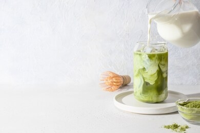 iced green matcha tea and pouring milk in glass on white background. space for text. close up. horizontal orientation.