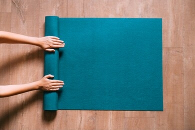 fit woman folding blue exercise mat on wooden floor before or after working out in yoga studio or at home. equipment for fitness, pilates or yoga, well being concept. flat lay, space for text.