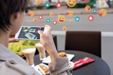 female blogger influencer hold phone take food mobile photo on phone sit at cafe table. girl vlogger shoot social media instagram post on smartphone get many likes emoji over shoulder closeup view.