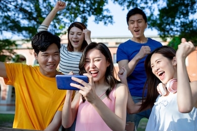 close up of happy young asian students are excited playing mobile game with smartphone on campus