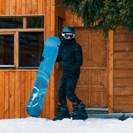 young man ready to snowboard. black costume on wooden background.