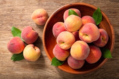 fresh ripe peaches with leaves in a bowl on a wooden table, top view