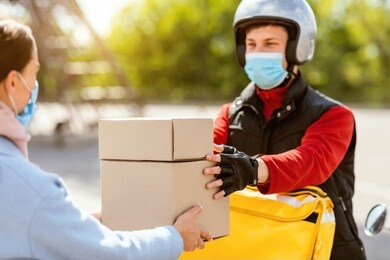 food delivery service. courier in medical mask giving lunch boxes to customer girl delivering restaurant meals on moto scooter outdoor.