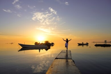 sunset on seaview at the pier with woman standing and boats floating in water, with reflections over colorful sky  background, bahrain.