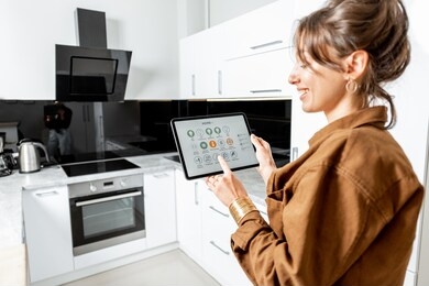 young woman controlling kitchen appliances with a digital tablet, mobile device with launched smart home application. smart home concept