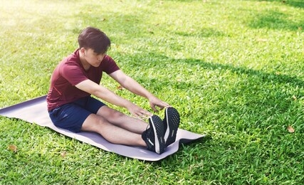 young asian sports male do stretching exercise or yoga in the park