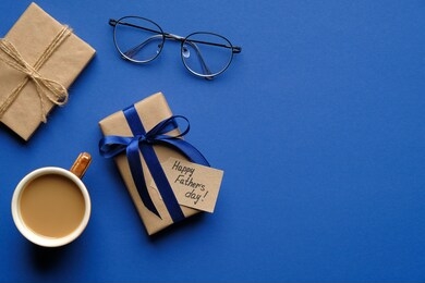 happy fathers day concept. flat lay composition with festive gift box, happy father's day inscription, cup of coffee and glasses on blue background. top view.