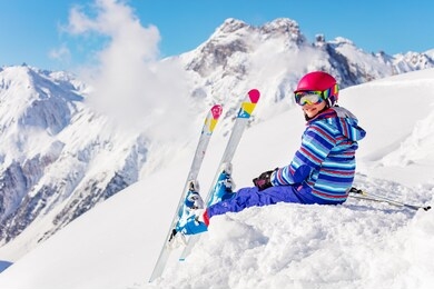 cute child in bright sport outfit sit on the snow pile in the mountain over high peaks look back to camera