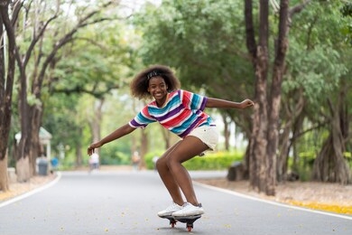 african american young girl having fun riding skateboard at summer outdoor. teenager girl practicing skateboarding in the park.