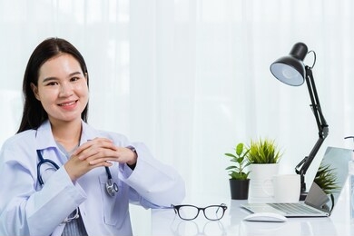 portrait asian confident female doctor working personal laptop computer at hospital office. thai woman medical expertise staff smiling sitting posing on desk space front computer, healthcare concept