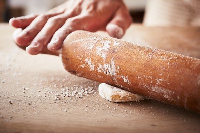 hands baking dough with rolling pin on wooden table