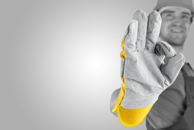 workman making a perfect gesture with his gloved hand with focus to his hand over a grey background with a highlight and copyspace.