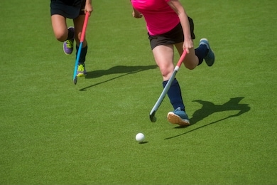 field hockey player, in possesion of the ball, running over an astroturf pitch, looking for a team mate to pass to