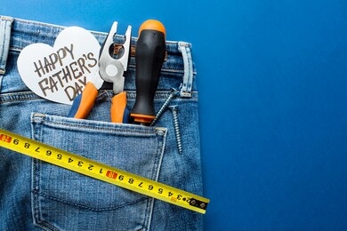 
trendy blue background with pliers, a screwdriver in the pocket of jeans and a heart with the inscription: "happy father's day." give a present to dad. happy fathers day concept.