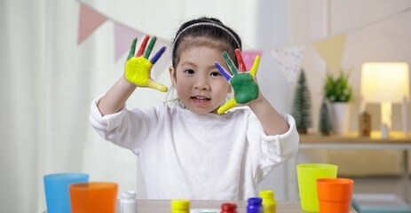 kid's creativity, child little asian girl hands painted in colorful paints in the class room at home, educational concept for school