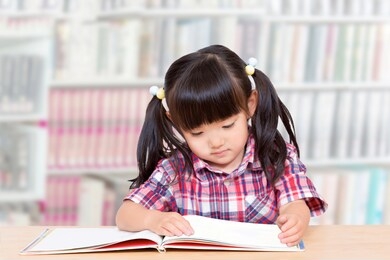 a little girl reading book in the library.