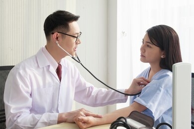 a young asian male specialist doctor uses stethoscope while respiratory examination, lung function, heartbeat of a female patient in the hospital room. healthcare and medical insurance concept.