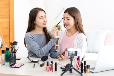 beautiful asian woman beauty vlogger doing cosmetic makeup demonstration with her friend at home