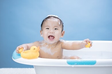 baby having bath in tub and playing with yellow duck on blue background