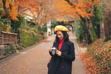 young happy asian woman looking to camera for checking picture and walking in beautiful autumn park, tokyo, japan, asia. lifestyle and travel concept