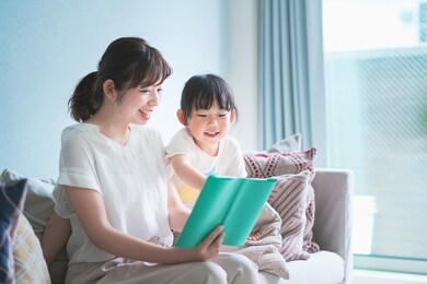 mother and daughter sitting on the sofa and reading a picture book