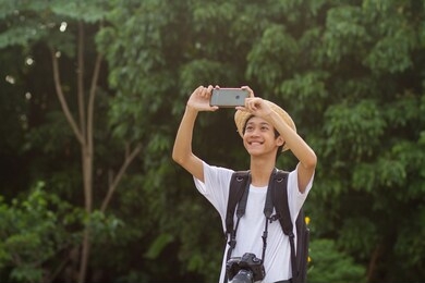 happy young teen of asian people taking picture with mobile phone while enjoy in green nature of tropical forest or public park.