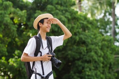 happy asian man with big backpack of camera gear enjoy in green nature of public park or tropical forest.